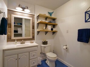 A bathroom with a wooden-framed mirror, white sink, and toilet. There are shelves with towels and a blue decorative item on the wall. - Make Memories and let Your Fun-family Fishing & Hunting Adventure Start Here (Freeport)