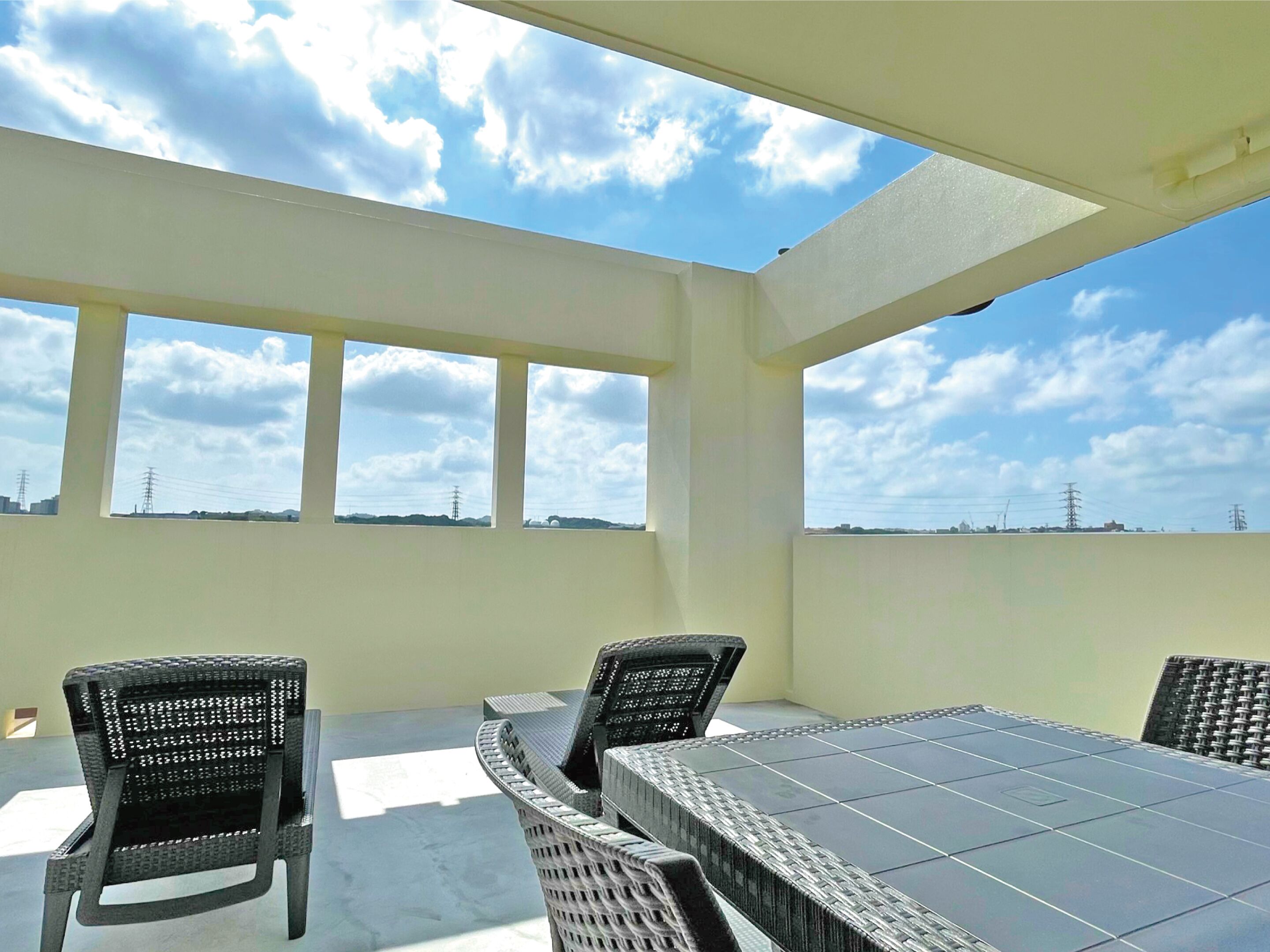 A covered outdoor seating area with a table and chairs, large windows, and a view of the sky and distant buildings.