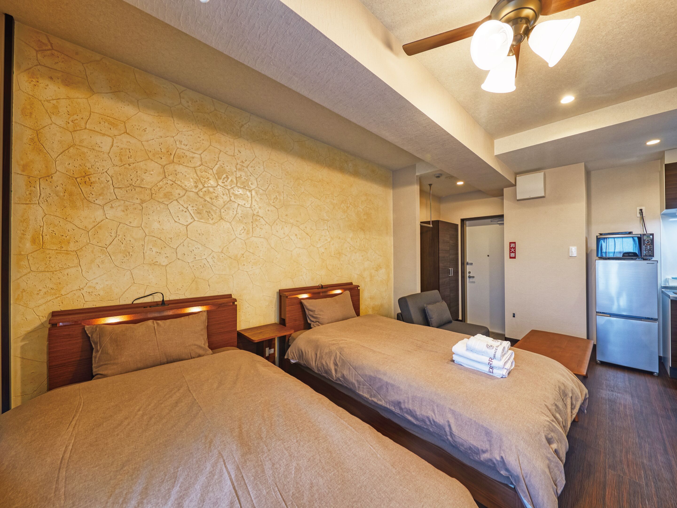 A hotel room with two beds, a kitchenette, and a bathroom.