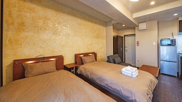 A hotel room with two beds, a kitchenette, and a bathroom.