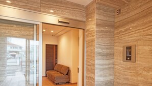 A modern elevator with a control panel, a plush seating area, and a glass door leading to a hallway. - Terrace Resort Mihama (Chatan)