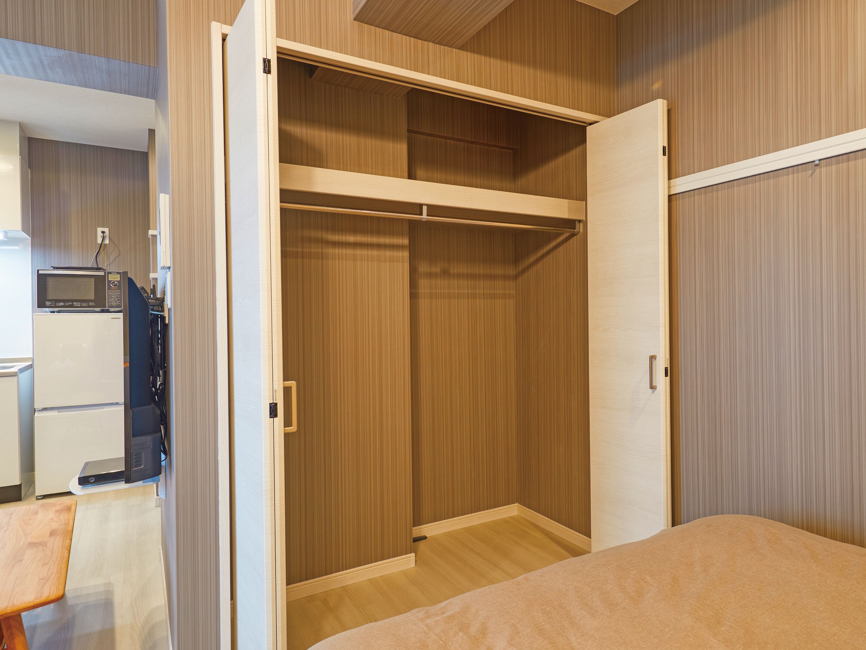 A bedroom with a wooden wardrobe, a bed, and a small desk with a microwave.