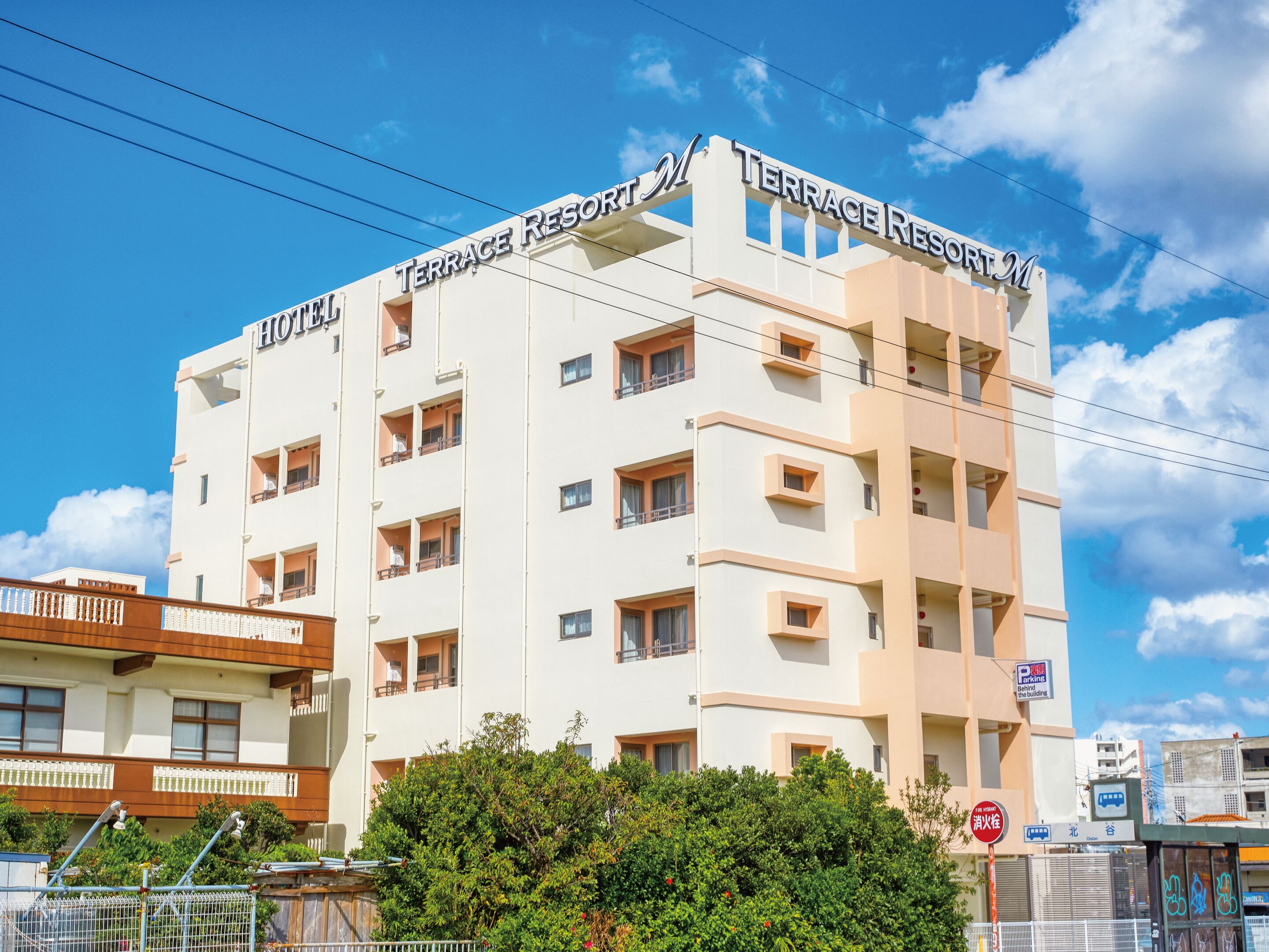 A multi-story hotel named "Terrace Resort M" with a modern architectural design, featuring balconies and a visible parking sign.