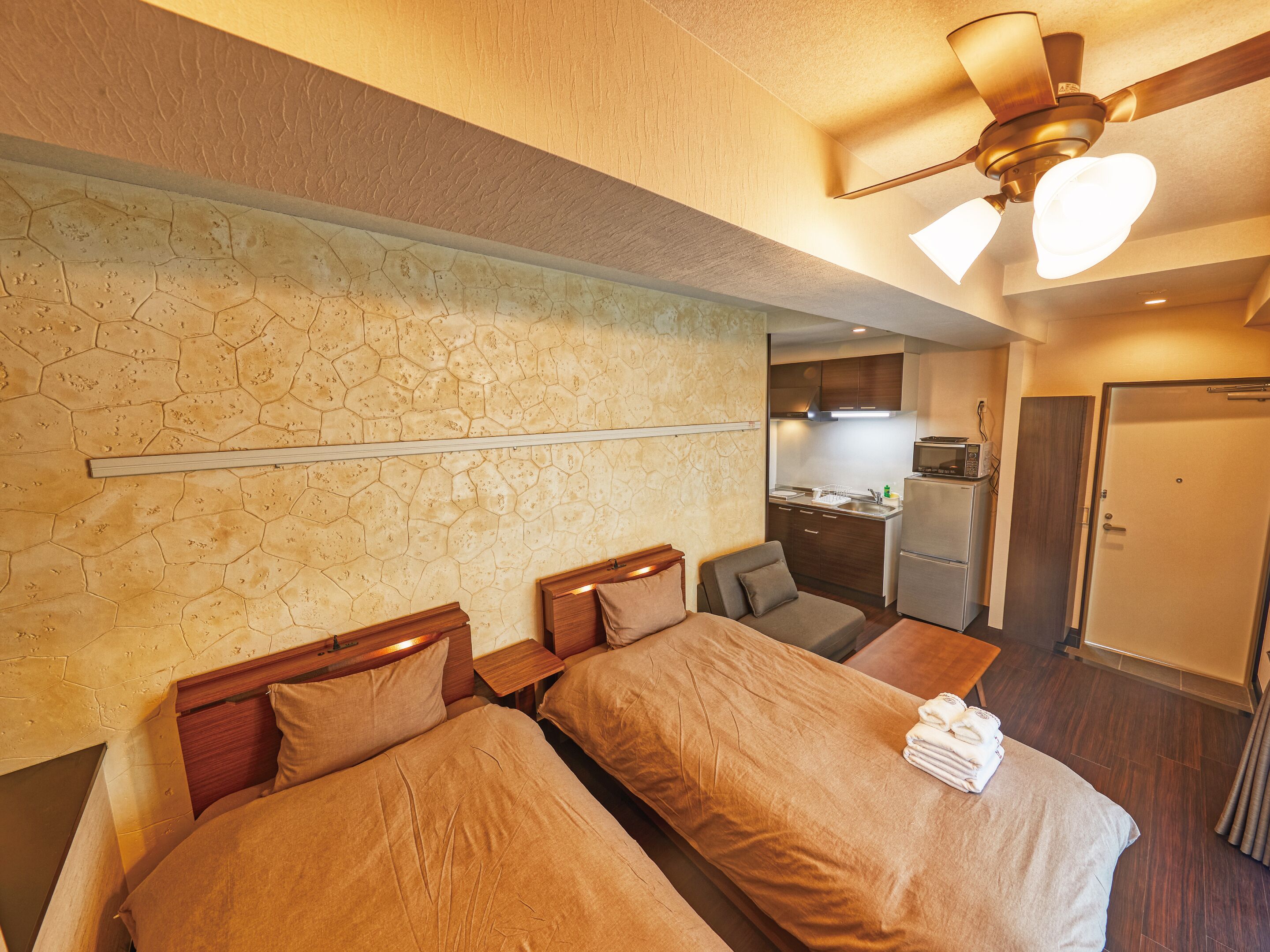 A hotel room with two beds, a kitchenette, and a ceiling fan.