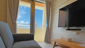 A modern living room with a grey sofa, a wooden coffee table, and a flat-screen TV mounted on the wall. - Terrace Resort Mihama (Chatan)
