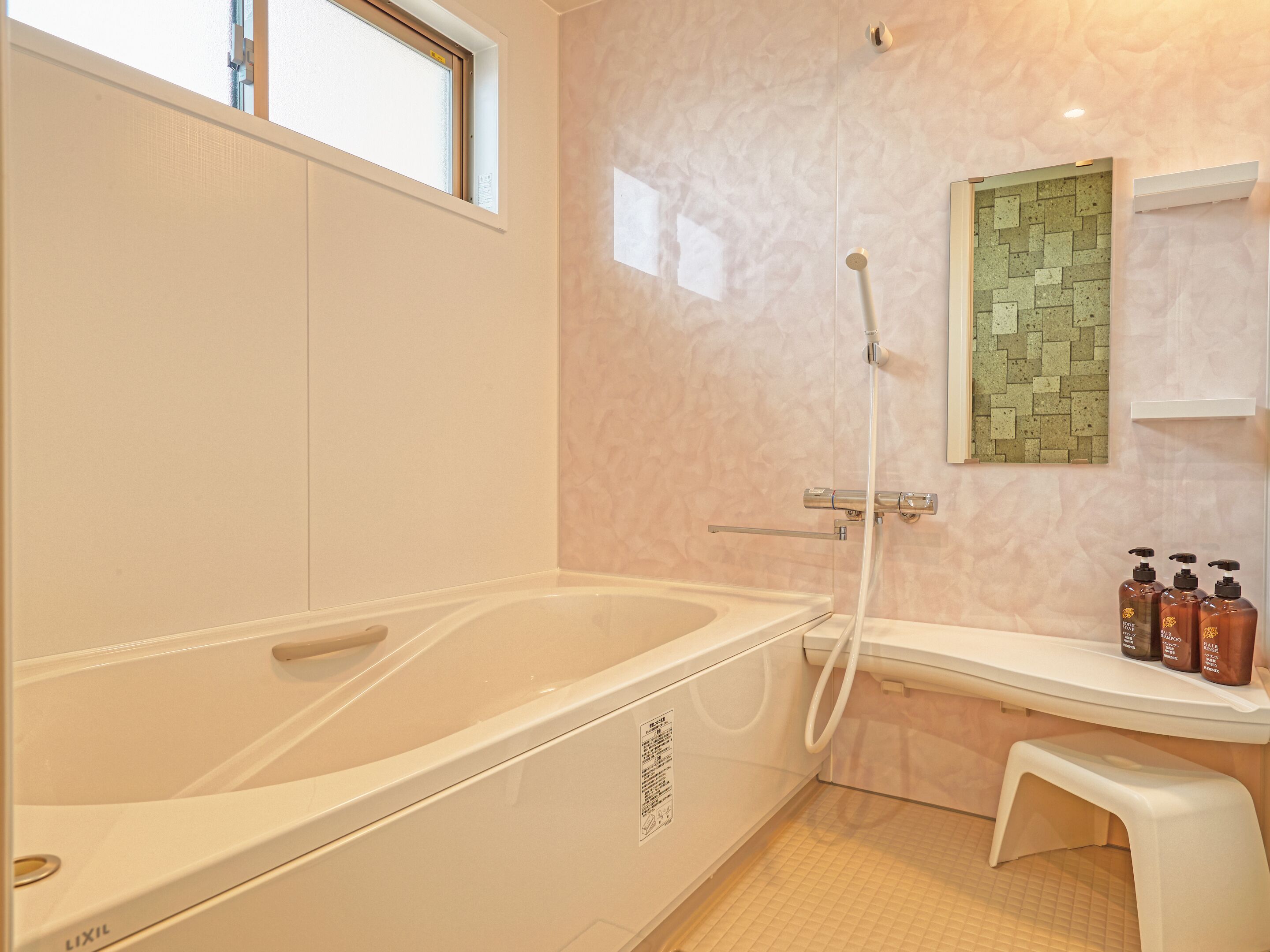 Un baño con bañera, ducha, un taburete pequeño y un estante con artículos de aseo.