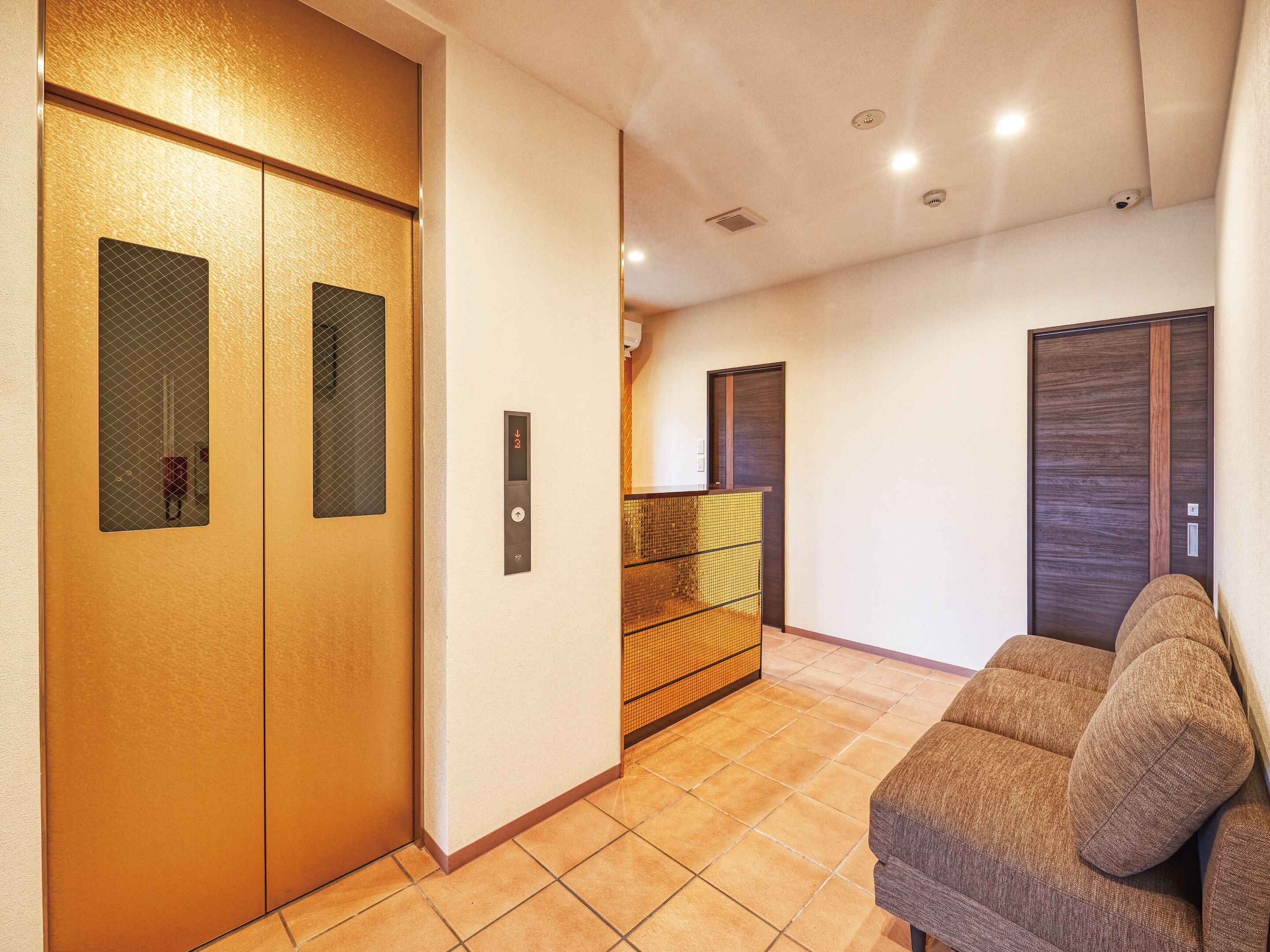 A hallway with two elevators, a sofa, and a tiled floor.