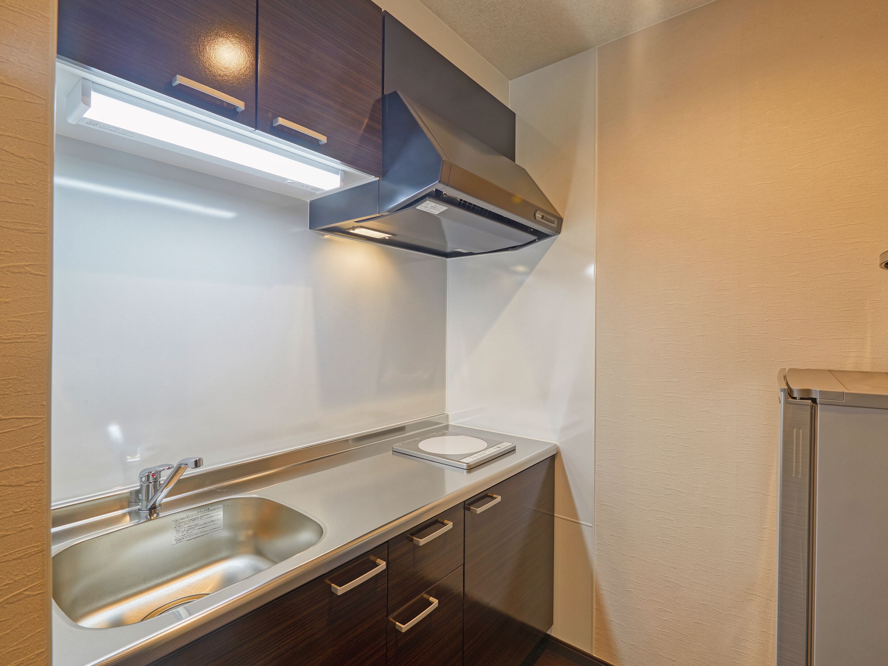 A modern kitchen with a stainless steel sink, wooden cabinets, and a built-in range hood.