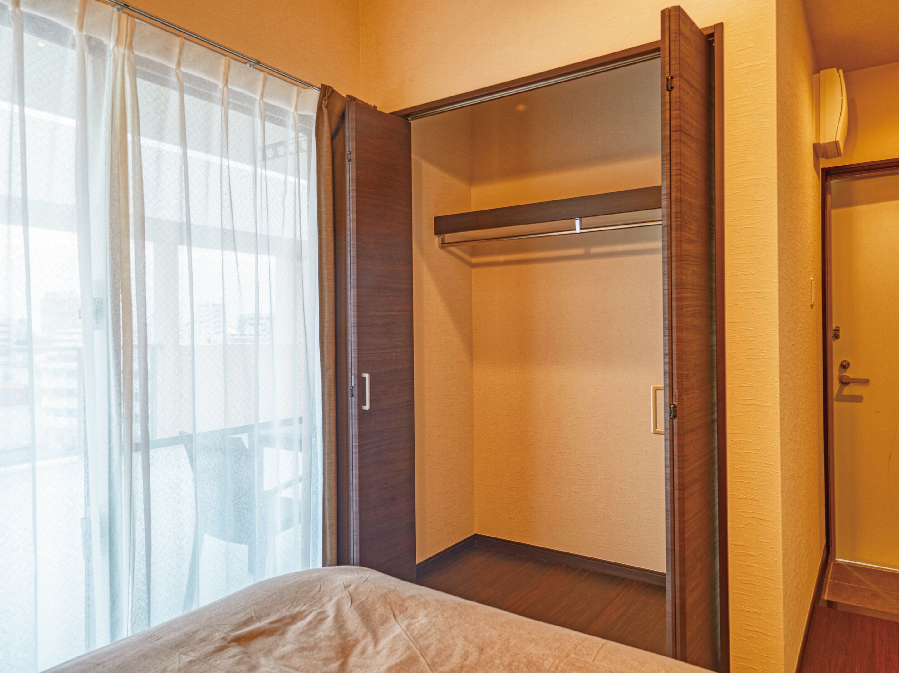 A bedroom with a bed, a closet with a sliding door, and a window with sheer curtains.