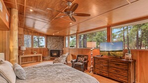 A spacious bedroom with a large bed, a fireplace, a television, and a stone wall. - Historic Ranch House, A/C, on forest acres, in town (Flagstaff)