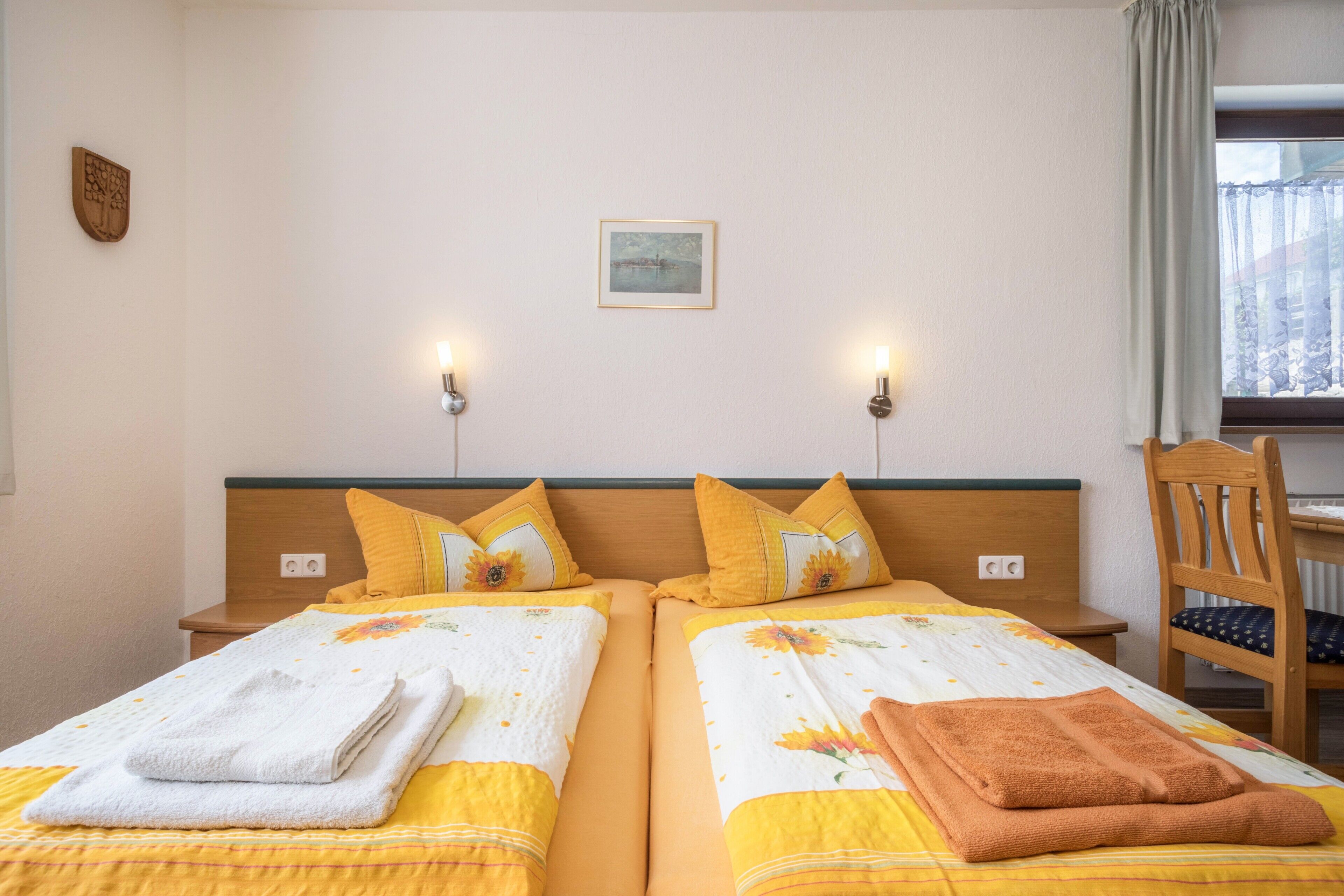 A hotel room with two beds, each with a headboard, pillows, and towels. There is a chair and a window with curtains.