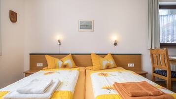 A hotel room with two beds, each with a headboard, pillows, and towels. There is a chair and a window with curtains.