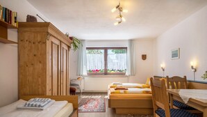Une chambre avec deux lits, une armoire en bois, un bureau avec une chaise, une fenêtre avec des rideaux et un radiateur.