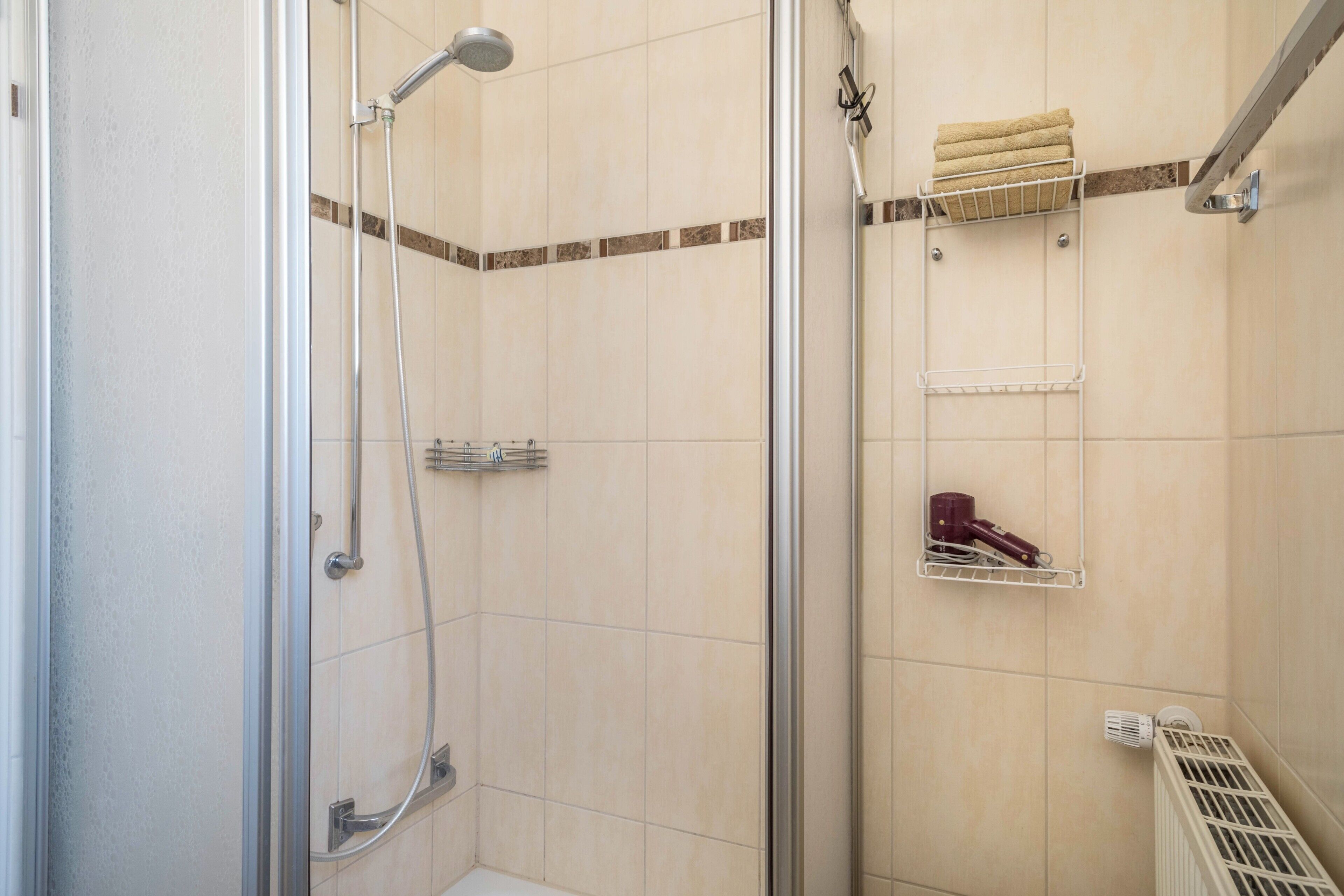 Eine Dusche mit Glastür, Handtuchhalter und Heizkörper.