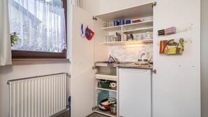 Une cuisine compacte dotée d’un réfrigérateur intégré, d’étagères où sont rangés la vaisselle et d’une fenêtre avec un rideau.