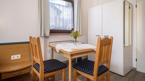Une pièce avec une table en bois, deux chaises, un radiateur, une fenêtre avec des rideaux et une armoire.