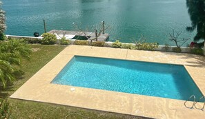 Piscina retangular com deck de madeira e vista para a água.