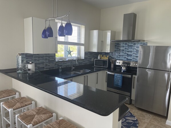 A modern kitchen with a black countertop, stainless steel appliances, and a blue backsplash.