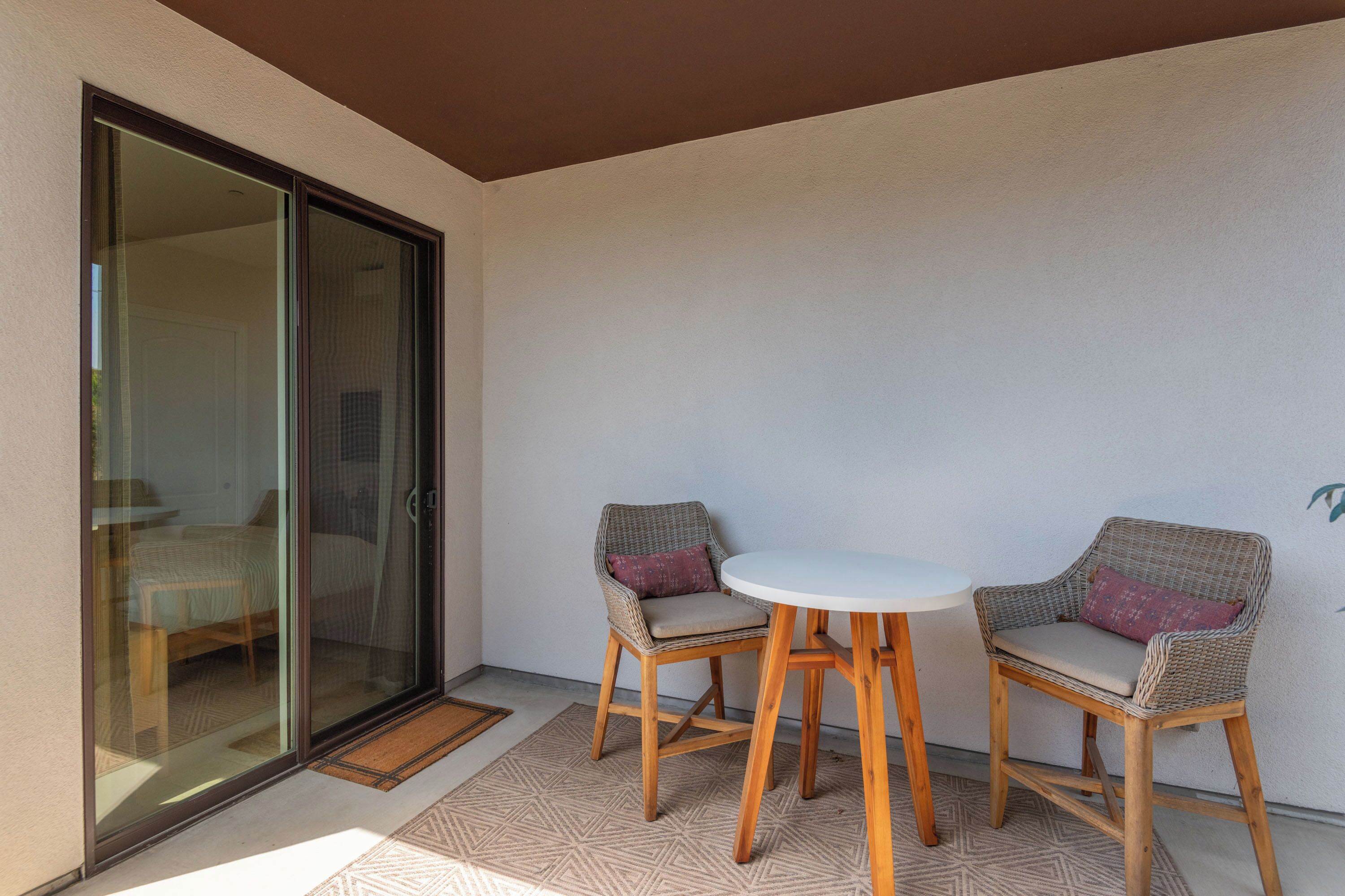 Un balcon avec deux fauteuils en osier, une petite table ronde et une porte-fenêtre coulissante donnant sur une chambre.