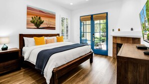 Une chambre à coucher comprenant un lit, une tête de lit en bois, des tables de chevet, un ventilateur de plafond et une vue sur l’extérieur par une porte.