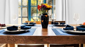 Une table à manger dressée avec des serviettes, des assiettes et des verres à vin bleus, et un vase de fleurs placé au centre.