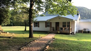 A house with a gravel path leading to the front door, surrounded by grass and trees. - Seek your rest at “Bertie’s Nest” (Parthenon)