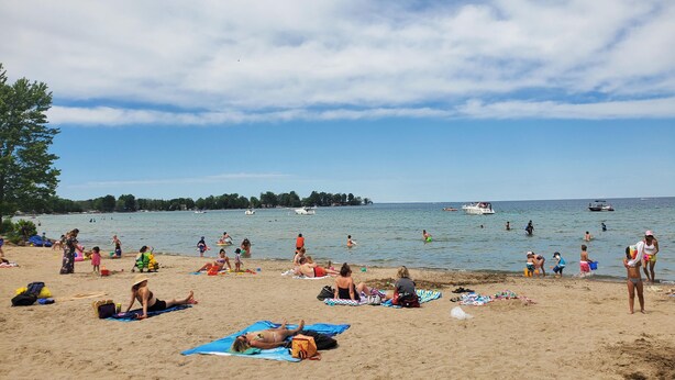 Une plage où l’on peut voir des gens se prélasser au soleil et nager, des bateaux sur l’eau et un ciel dégagé.