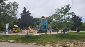 Une aire de jeux dotée de diverses structures ludiques, de bancs et d’un panneau d’information.