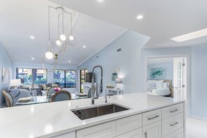 Une cuisine moderne dotée d’un grand îlot central, d’appareils électroménagers intégrés et de luminaires suspendus.