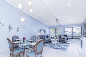 Un salon moderne avec un coin repas, de grandes fenêtres et un ventilateur de plafond.