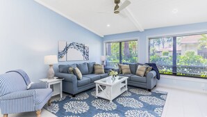Un salon avec un canapé bleu, un fauteuil à rayures, une table basse blanche et un ventilateur de plafond.