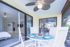 A room with a dining table set for two, a ceiling fan, and a bed with a white headboard. - Beach Paradise, Pool/Spa, Bright Updated Condo (Sarasota)