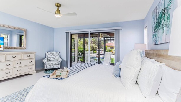 A bedroom with a bed, a dresser, a chair, a ceiling fan, and a view through a glass door. - Beautifully Renovated Bright Condo, Heated Pool, Tennis Courts, Putting Green, Ready to Book! (Sarasota)