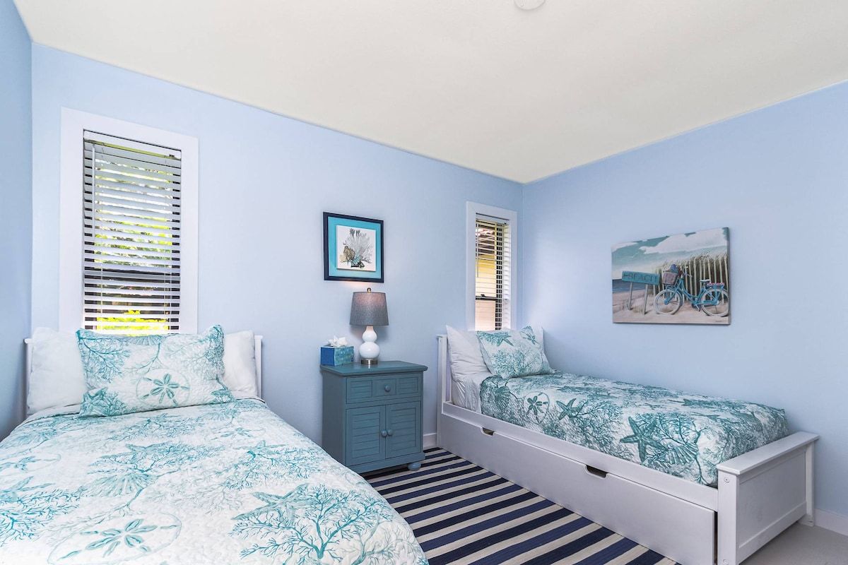 A bedroom with two beds, a nightstand, a lamp, and a framed picture on the wall.