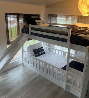 A bunk bed with a small slide leading to a balcony, white walls, and a view of the outdoors. - Lake of Egypt Cove - Waterfront Home, Kayaks, Pet Friendly (Creal Springs)