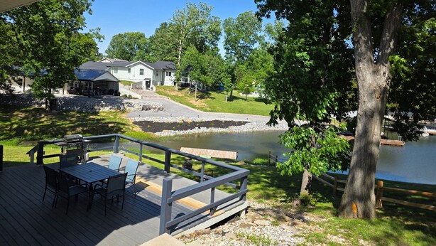 A deck with outdoor furniture, a pond, and houses in the background. - Lake of Egypt Cove - Waterfront Home, Kayaks, Pet Friendly (Creal Springs)