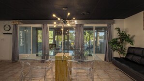 A modern living room with a glass dining table, clear chairs, a black sofa, and a ceiling light fixture. - Lake of Egypt Cove - Waterfront Home, Kayaks, Pet Friendly (Creal Springs)