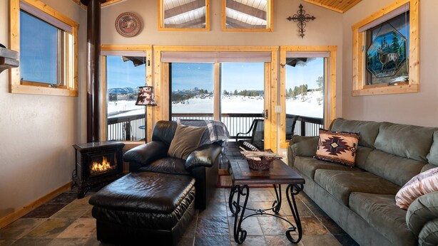 A cozy living room with a fireplace, leather furniture, and large windows offering a snowy mountain view.