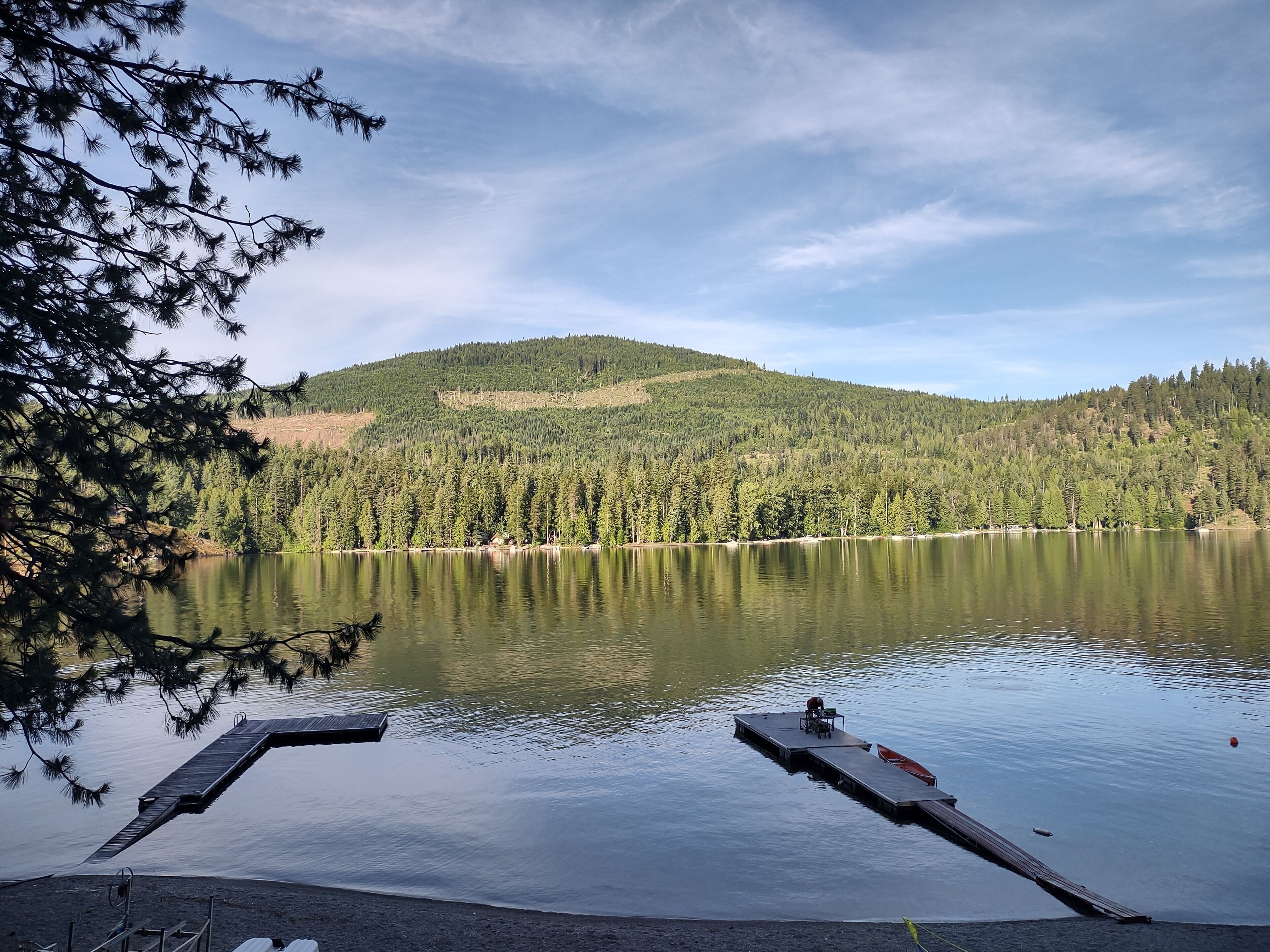 Un lac paisible, avec une jetée qui s’avance sur l’eau, entouré d’une forêt dense et dominé, au loin, par une colline.