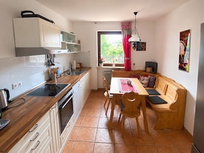 A compact kitchen with a dining area, wooden cabinets, a built-in oven, and a window with a view.