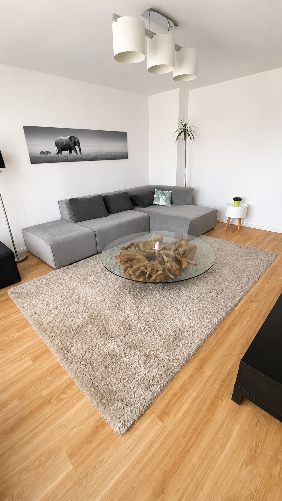 Un salón moderno con un sofá gris, una mesa de centro redonda de cristal y un cuadro grande en la pared.
