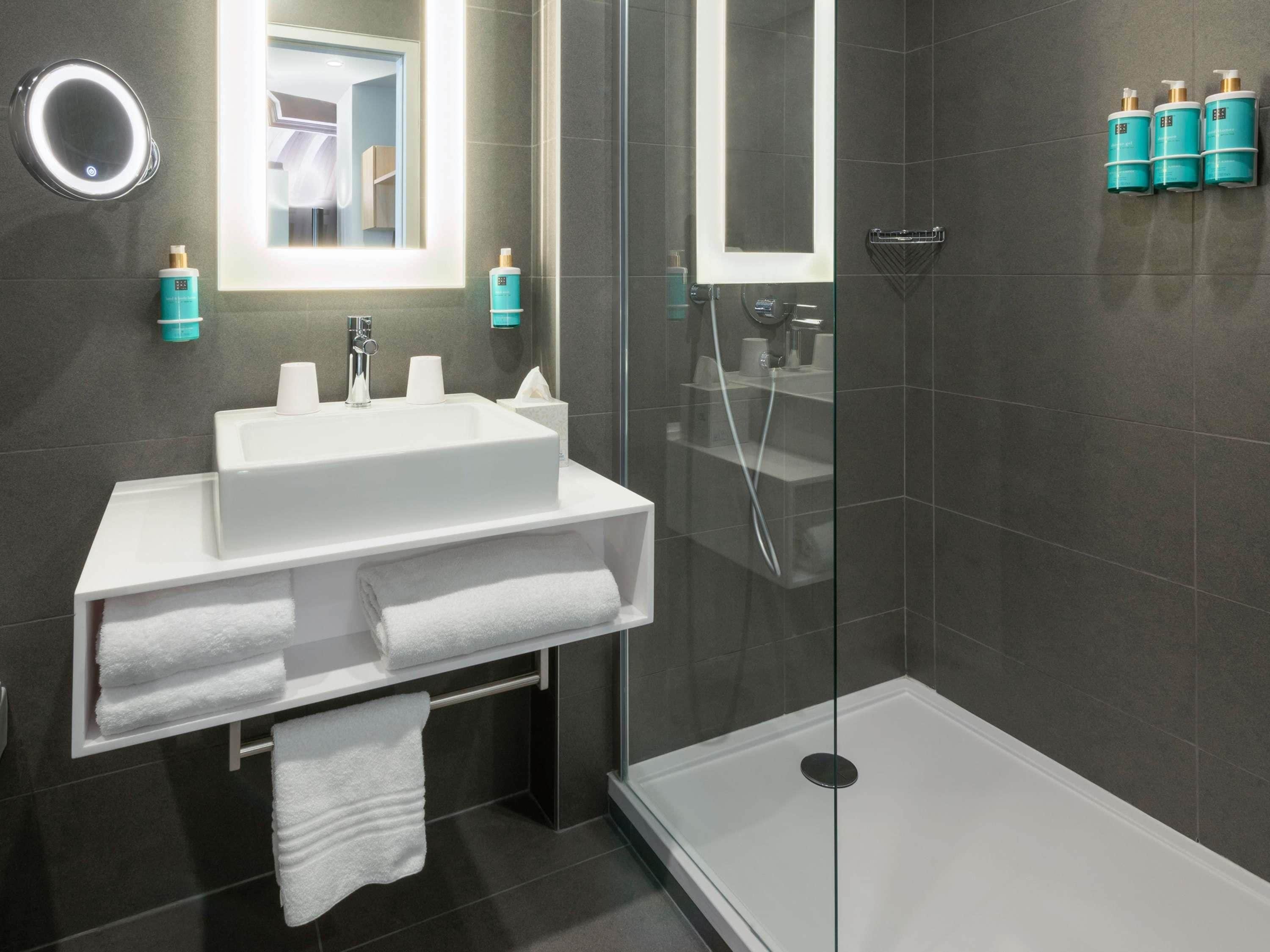 Un baño moderno con cabina de ducha de vidrio, un lavabo blanco con espejo y artículos de aseo en la pared.