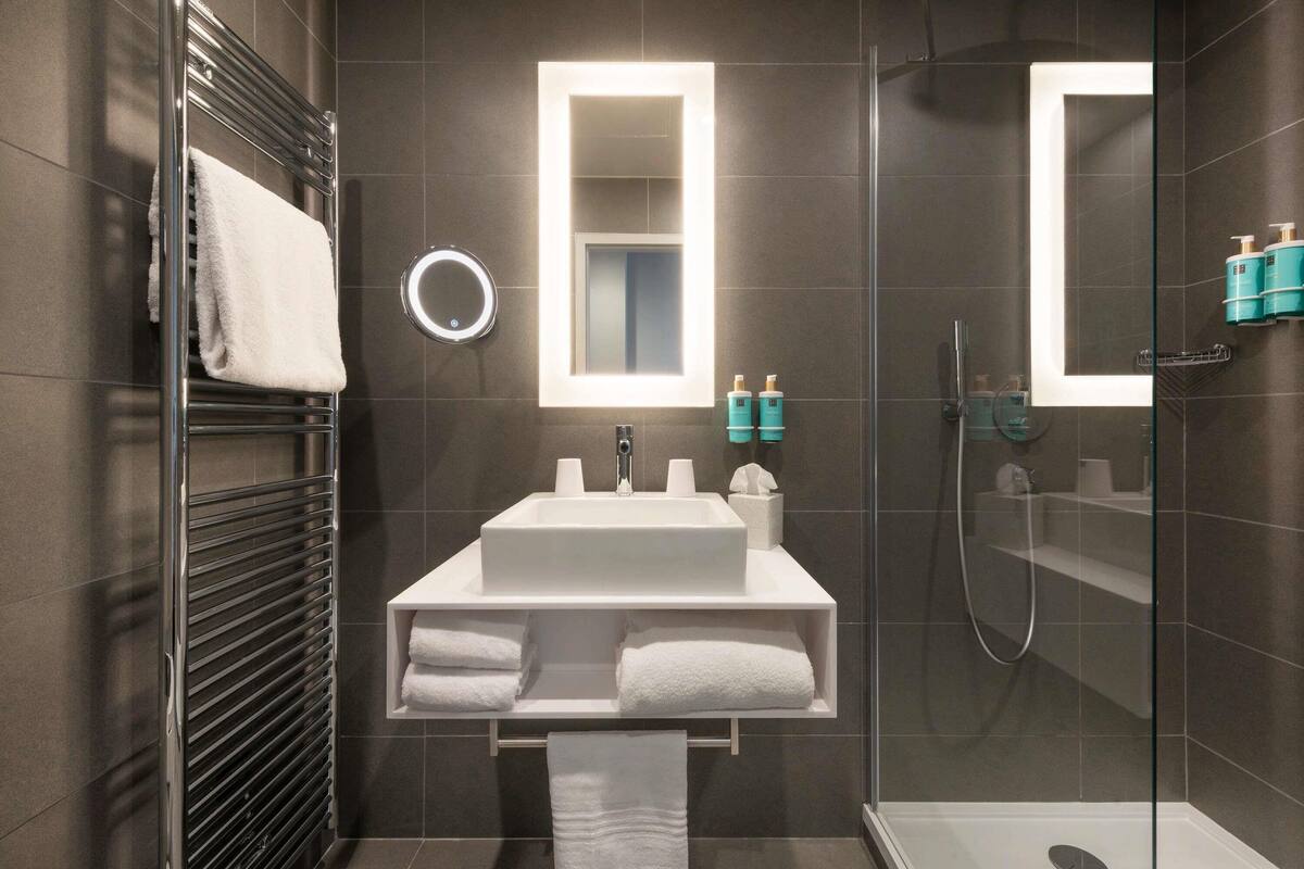 A modern bathroom with a glass shower enclosure, a white sink, and a mirror above it.