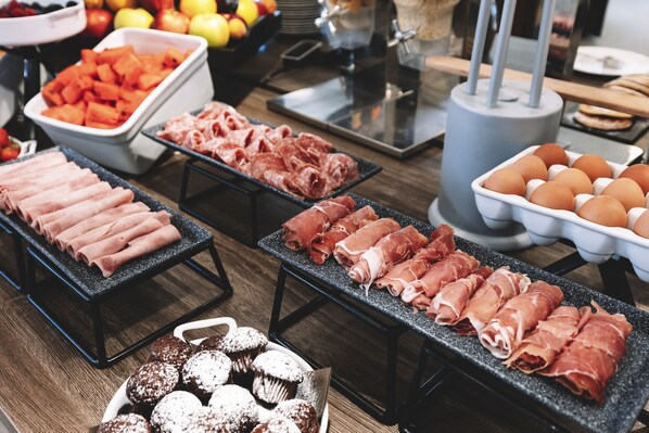 Un buffet proposant une variété de plats, notamment des viandes, des fruits et des pâtisseries.