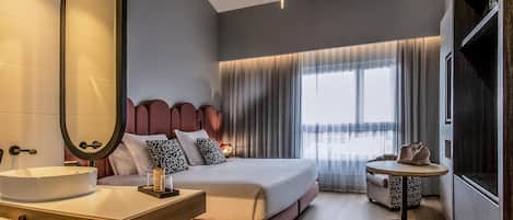 Habitación de hotel moderna con una cama grande, mesita de noche, espejo y una pequeña mesa redonda con una silla.