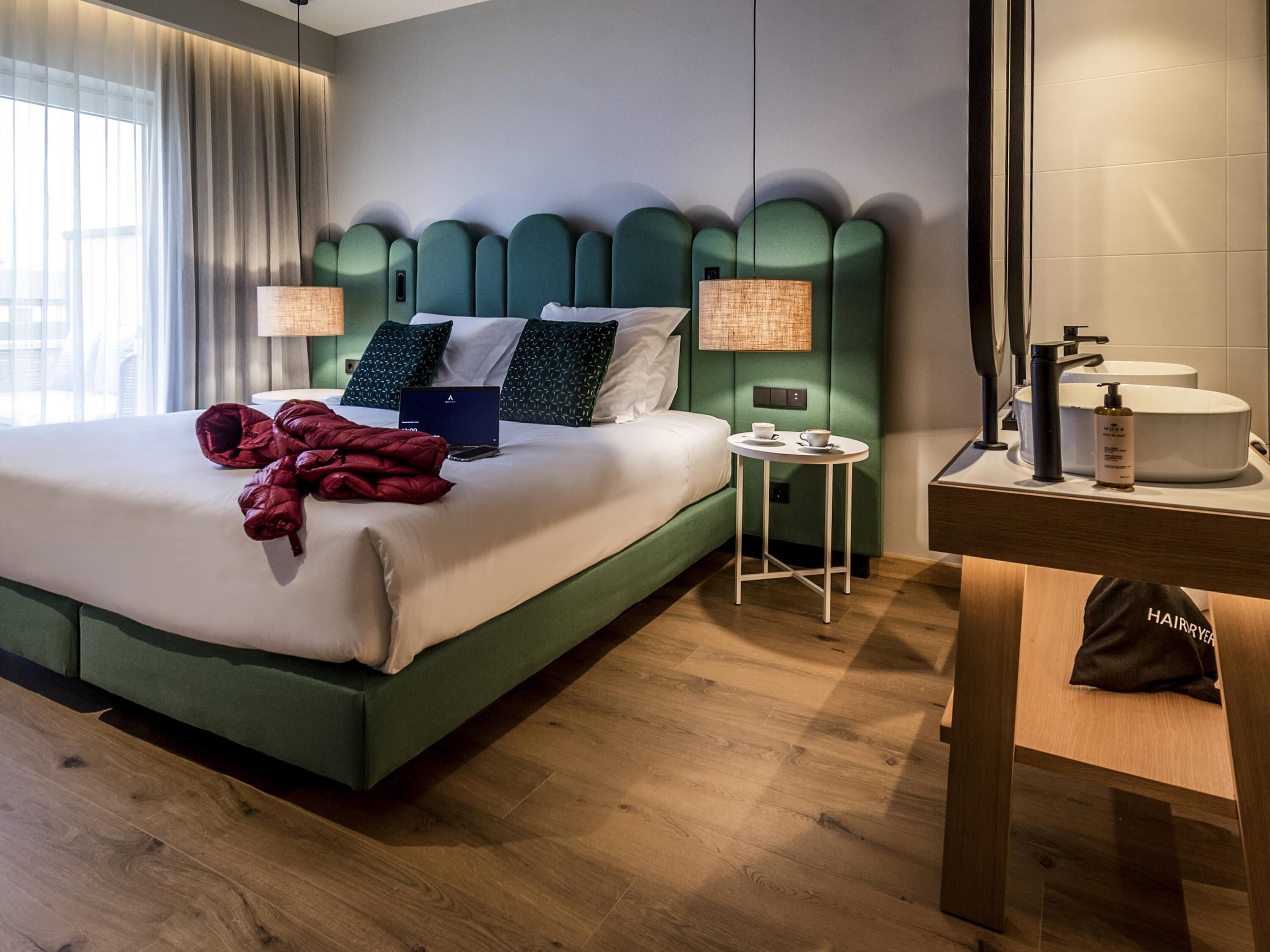Et hotelværelse med seng, sengeborde, en lille bord, et spejl og et badeværelse med toiletartikler.