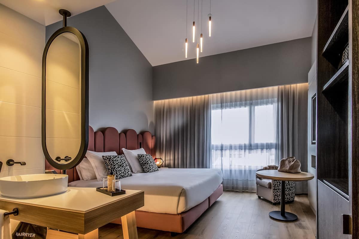 A modern hotel room with a large bed, bedside table, and a round table with a chair.