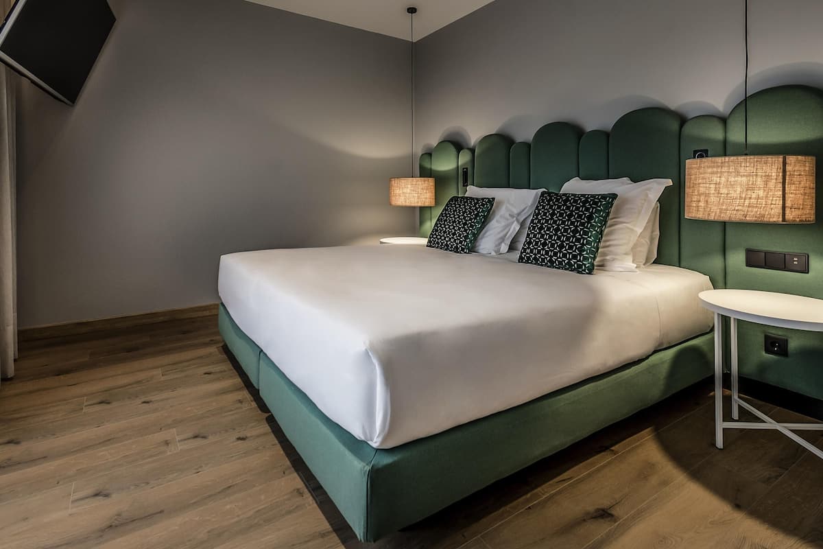 A modern hotel room with a large bed, a small round table, and a television mounted on the wall.