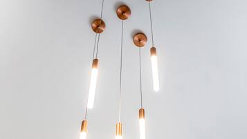 Een plafond met een moderne lamp, bestaande uit meerdere hanglampen en koperkleurige details.