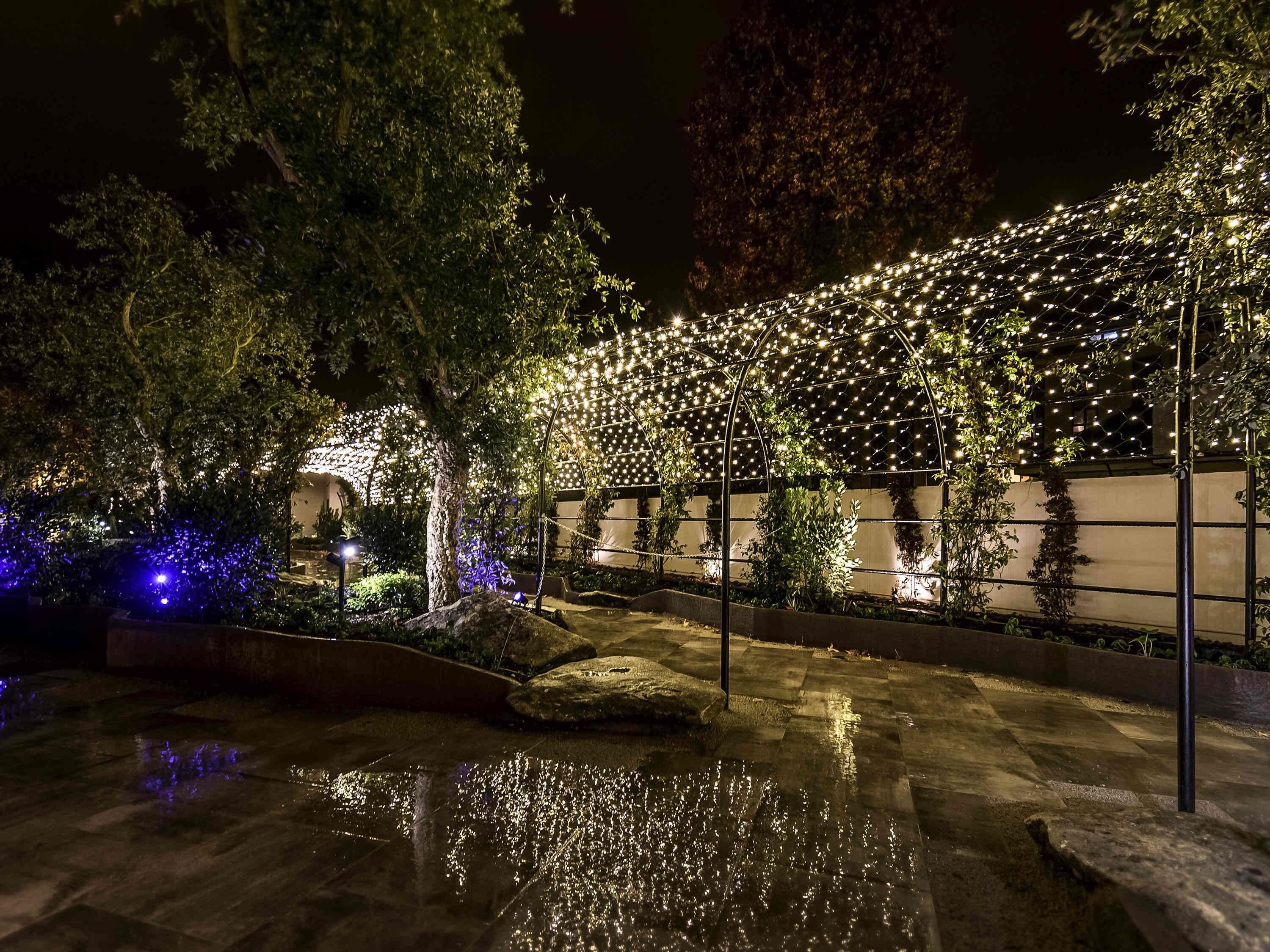 A nighttime outdoor area with a water feature, stone steps, and string lights.